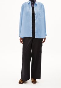 Light blue long-sleeve shirt with a front pocket, paired with loose black trousers and leopard-print slip-on shoes.