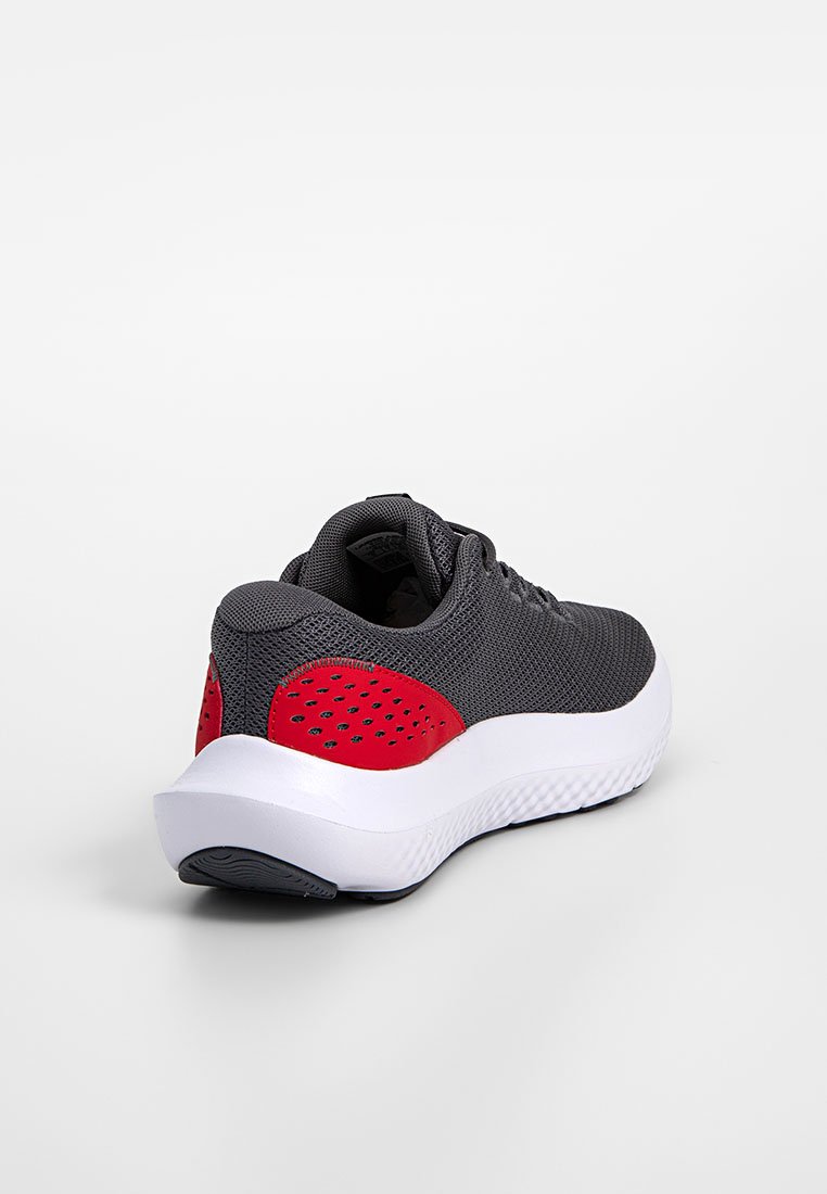 Zapatilla deportiva gris con parte superior de malla texturizada, acento rojo en el talón y suela blanca acolchada. Presenta un diseño elegante y redondeado.