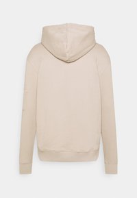 Beige kapuce džemperis ar mīkstu kokvilnas maisījumu, ar kangarū biksēm un ribotām piedurknēm. Minimālistisks dizains un gluda faktūra.