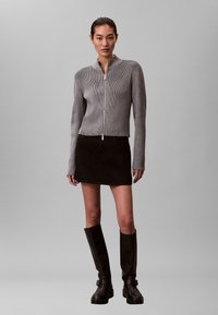 Szary sweter rozpinany na zamek z dzianiny o prążkowanej fakturze, zestawiony z czarną mini spódnicą jeansową i czarnymi skórzanymi kozakiem za kolano.