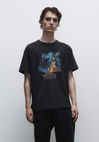 Sort bomulds T-shirt med et farverigt "Star Wars" grafisk tryk på forsiden, der viser ikoniske karakterer og rumelementer.
