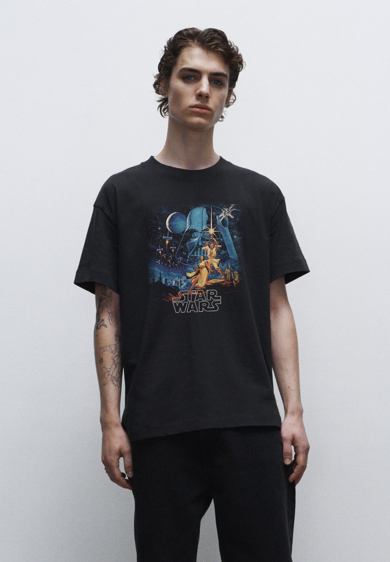 Sort bomulds T-shirt med et farverigt "Star Wars" grafisk tryk på forsiden, der viser ikoniske karakterer og rumelementer.
