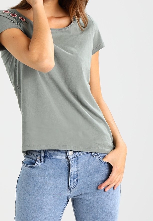 Lys grøn bomulds t-shirt med rund halsudskæring, korte ærmer og blomsterbroderi på skulderen. Bæres med blå jeans.
