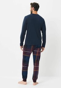 Marineblauses mit langen Ärmeln kombiniert mit bordeauxroten Karotten-Pyjama-Hosen, die mit weißen und goldenen Akzenten versehen sind und aus einem weichen Stoff bestehen. Entspannte Passform, elastische Bündchen.