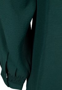 Camicia a maniche lunghe verde scuro con tessuto testurizzato, polsini arricciati e vestibilità rilassata, caratterizzata da un design semplice e senza ornamenti.