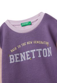 Felpa viola con accenti rosa chiaro, caratterizzata da un logo grafico "BENETTON" e dal testo "BACK TO THE NEW GENERATION". Tessuto morbido, collo rotondo.