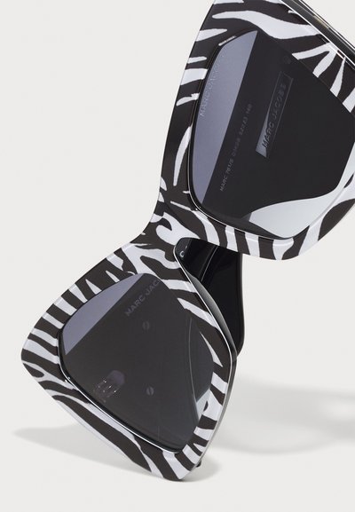 Marc Jacobs zonnebrillen met oversized, driehoekige frames in zwart-wit zebra print, met donkergetinte lenzen en metallic accenten.