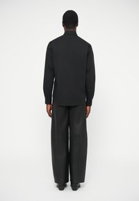 Camisa negra de manga larga y pantalones de pierna ancha hechos de tela suave. La camisa presenta un cuello con solapa y puños abotonados.