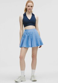 Tengerészkék, V nyakú, galléros crop top, amelyet egy világoskék rakott szoknyával párosítanak. A modellen fehér sportcipő és bokáig érő zokni található.