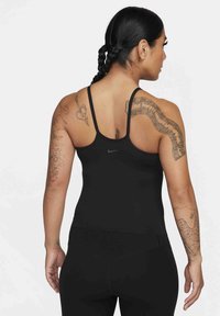 Black athletic tank top with thin straps and a fitted design. Features a small Nike logo on the back and intricate tattoos on the arms.