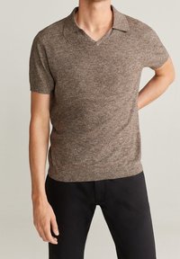 Béžový polo tričko s krátkým rukávem, texturovanou pleteninou, designem do V a klasickým límečkem, nošený s černými kalhotami.