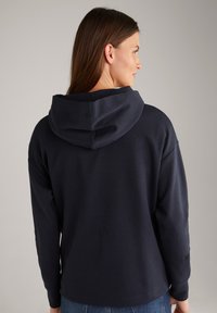 Felpa con cappuccio blu navy, dal fit rilassato, maniche lunghe e polsini a costine, caratterizzata da una texture liscia e priva di motivi o decorazioni visibili.