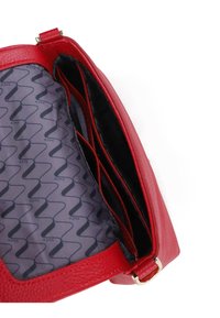 Červená kožená kabelka s texturovaným povrchem. Vnitřek obsahuje černě podloženou přihrádku se vlnitým vzorem a několika kapsami.