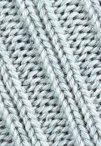 Primo piano di un morbido tessuto grigio lavorato a maglia con modelli di coste diagonali e punti torcigliati.