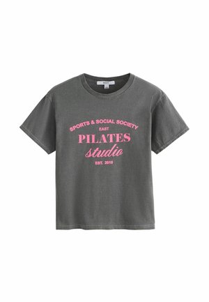 Mørkegrå T-shirt med korte ærmer og pink tekst foran, der lyder "SPORTS & SOCIAL SOCIETY EAST PILATES studio EST. 2010".