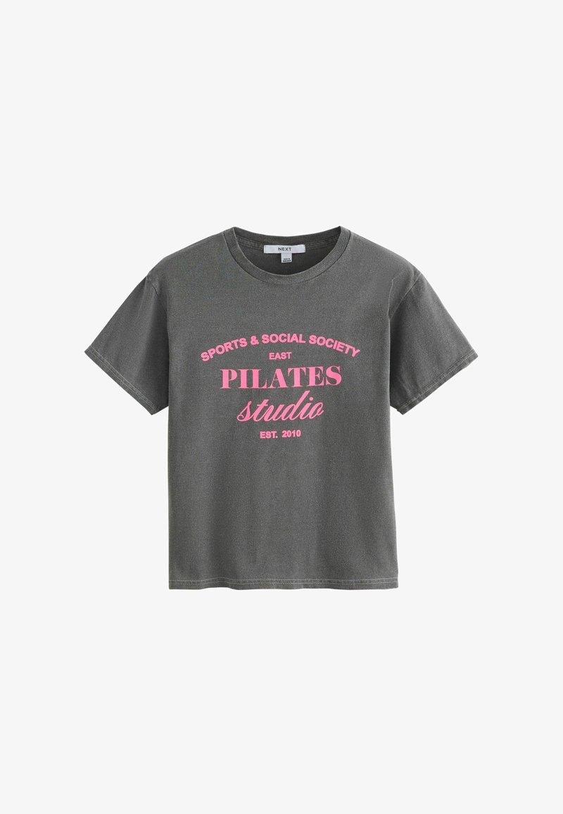 T-shirt gris foncé à manches courtes avec texte rose sur le devant indiquant "SPORTS & SOCIAL SOCIETY EAST PILATES studio EST. 2010".