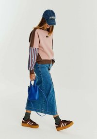 Ružová a hnedá farbou blokovaná mikina so pruhovanými rukávmi, skombinovaná s dlhou džínsovou sukňou, hnedými teniskami a modrou kabelkou.