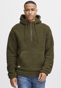 Olive green fleece hoodie with a zippered neck, kangaroo pocket, and textured surface. Features drawstrings and logo tag at the hem.