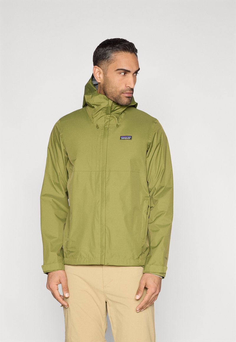 Ελαφρύ πράσινο αδιάβροχο με κουκούλα, με φερμουάρ μπροστά, ελαστικές μανσέτες και ένα μικρό λογότυπο στο στήθος. Ομαλή υφή.