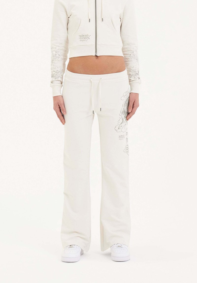 Witte cropped hoodie met voorzak en ingewikkelde ontwerpen op de mouwen, gecombineerd met bijpassende witte sweatpants met grafische print.