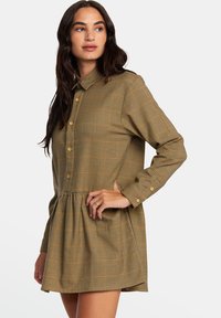 Vestido de manga larga a cuadros en tonos marrones tierra, con cuello abotonado y cintura fruncida, que presenta una falda de corte holgado.