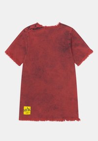 T-shirt vermelho de manga curta com bainha desfiada, textura de lavagem vintage e uma etiqueta amarela no canto inferior esquerdo.