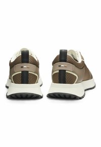 Pari urheilusnekkereitä, joissa on ruskeaa ja vaaleaa verkkomateriaalia, mustia pystyraitoita ja valkoiset pohjat, nähtynä takaa valkoista taustaa vasten.