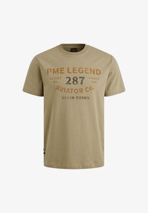 Camiseta de algodón beige con cuello redondo, mangas cortas y texto impreso en marrón y negro. El diseño incluye información de la marca y del vuelo.