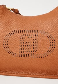 Borsa a mano in pelle marrone con finitura testurizzata, caratterizzata da un design ovale perforato e dettagli in hardware dorato.