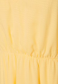 Žluté šaty s texturovanou tkaninou a jemným diamantovým vzorem, s přiléhavým tělem a shromážděnými detaily v pase.