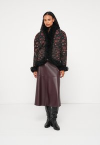 Kvadrična črna jakna s cvetličnim vzorcem, ovratnikom iz krzna in manšetami, v kombinaciji z bordo usnjeno midi krilom in črnimi škornji do kolen.