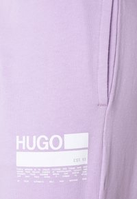 Lila sweatshirt med ribbat mönster, en framträdande vit logotyp och en etikett med texten "EST. 93" på framsidan. Enkelt design med korta ärmar.