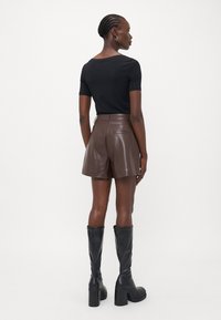 Haut noir à manches courtes, short taille haute en simili cuir marron, bottes à plateforme noires montant jusqu'aux genoux. Texture lisse, design ajusté.