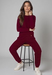 Set da lounge bordeaux realizzato in tessuto morbido, composto da una maglia a girocollo e pantaloni jogger. Sneakers bianche completano il look casual.
