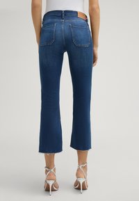 Niebieskie dżinsy o kroju wykończonym dzwonowatym, z postrzępionym brzegiem, dwiema tylnymi kieszeniami i znakowanym, brązowym skórzanym naszywką na talii.