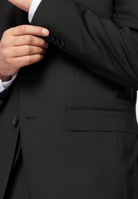 Czarna marynarka o gładkiej fakturze, z jedną kieszenią po boku i czterema guzikami na mankiecie. Dopasowany krój.