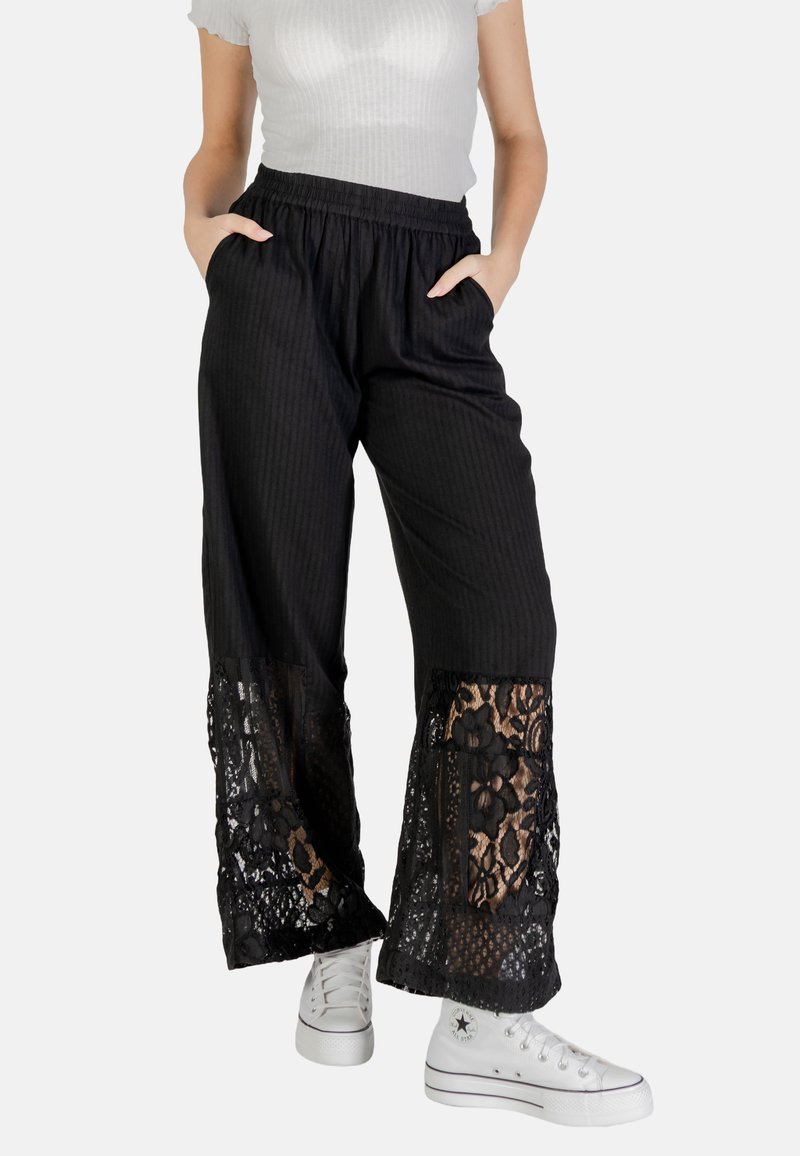 Pantaloni neri a gamba larga con texture a righe e sovrapposizione di pizzo all'orlo. Vita elasticizzata e tasche. Abbinati a scarpe da ginnastica bianche.