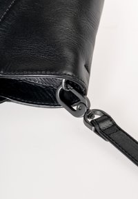 Zwarte leren clutch met ritssluiting, een gladde textuur en een afneembare band met zilverkleurige hardware.