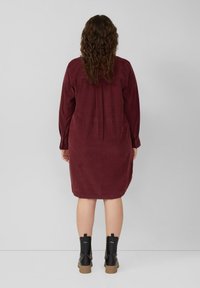 Burgundowa sukienka z korduroju z długimi rękawami, detalem w postaci plis w tylnej części oraz bocznymi rozcięciami. Nosi się z czarnymi botkami za kostkę z grubą podeszwą.