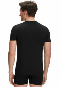 Schwarzes T-Shirt mit kurzen Ärmeln aus weicher Baumwolle; figurschmeichelndes Design, Rundhalsausschnitt, glatte Textur; kombiniert mit schwarzen Shorts.