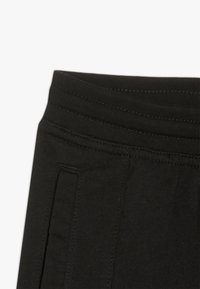 Black cotton joggers with a wide elastic waistband, featuring side pockets and textured stitching along the waist.