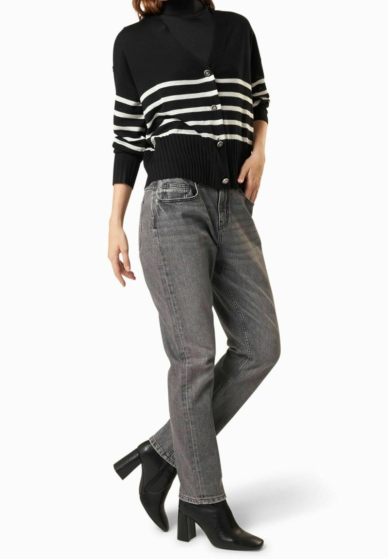 Cardigan a righe bianche e nere con bottoni, abbinato a jeans grigi a vita alta e stivaletti neri con tacco a blocco.