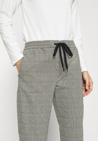 Grå rutig byxor med elastisk midja och snöre. Har en texturerad tyg och sidofickor. Avslappnad och löst sittande design.