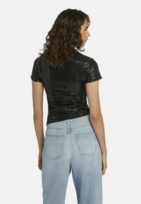 Zwart pailletten top met korte mouwen en een aansluitend ontwerp. Heeft een gestructureerd glanzend oppervlak en is gecombineerd met lichtblauwe high-waisted denim jeans.