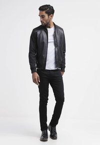 Melnas ādas bombers jaka ar ribotiem manžetēm, kombinēta ar baltu T-kreklu un melnām šaurām biksēm. Spīdīgas melnas kurpes ar mežģīnēm noslēdz izskatu.