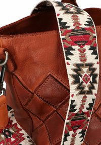 Borsa in pelle marrone con una texture trapuntata, dotata di una tracolla a motivi nei colori crema, rosso e nero, che presenta disegni geometrici.