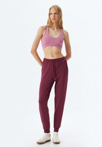Lichtroze sportbeha met een gecontourneerd design, gecombineerd met losvallende bordeauxrode joggers met een elastische tailleband en cuffed enkels.