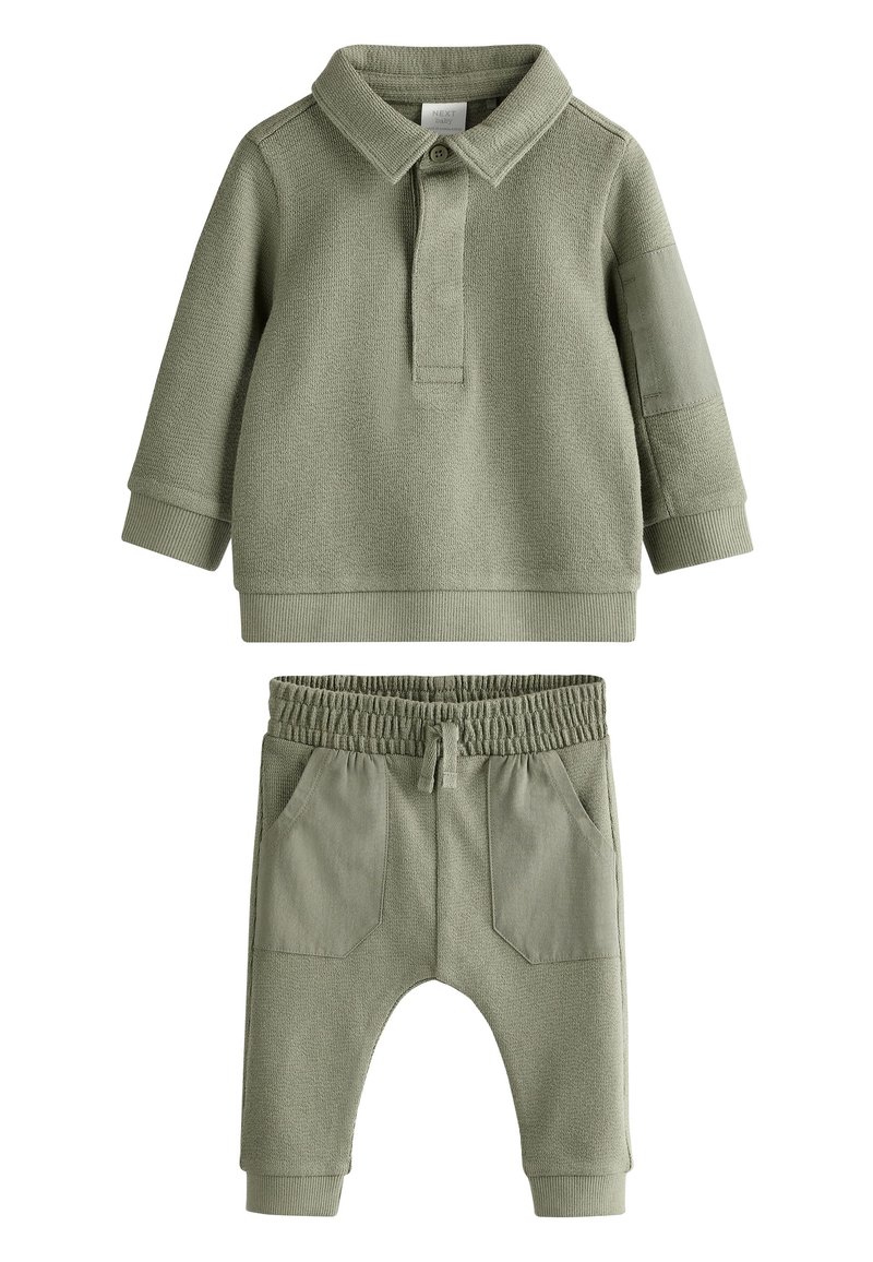 Gaiši zaļš divdaļīgs komplekts, kurā ietilpst teksturēta polo krekls ar garām piedurknēm, apkakli un pogu, kā arī elastīga vidukļa bikses ar kabatām.