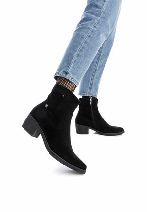 Stivaletti neri in suede con tacco quadrato, punta affilata, cerniera laterale e cuciture decorative. Indossati con jeans azzurri e calze in rete.