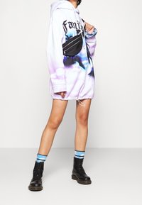 Felpa oversize viola e bianca con stampa floreale, orlo con coulisse e marsupio nero. Abbinata a stivali neri e calze a righe blu.
